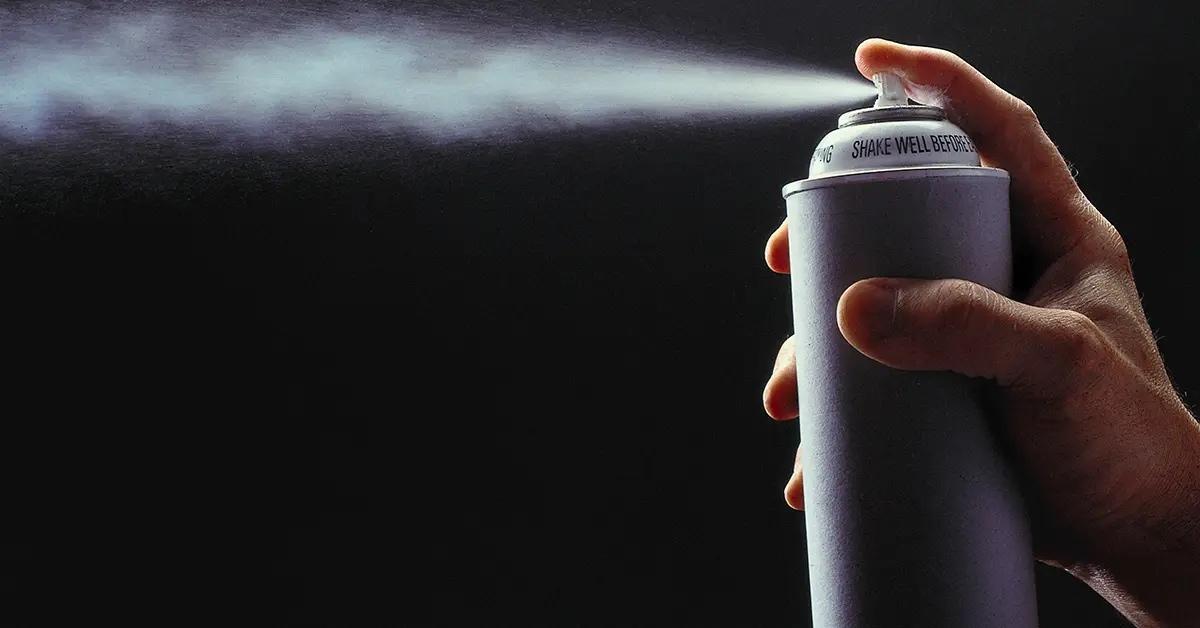 A hand holding an aerosol can that is spraying. 