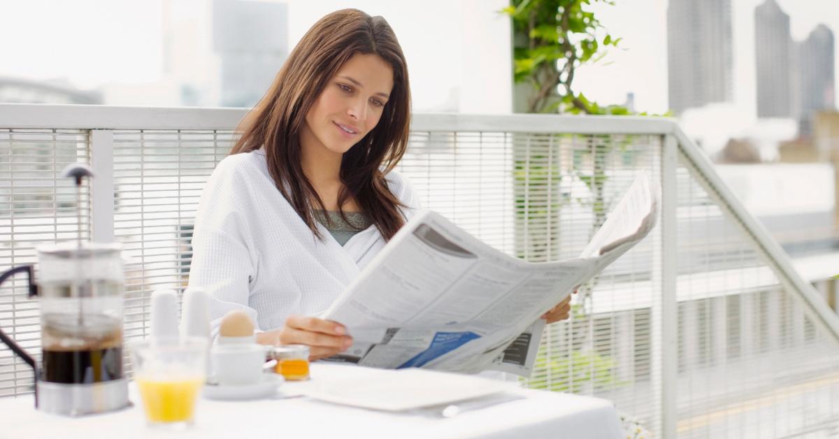 Woman reading newspaper and having breakfast on balcony