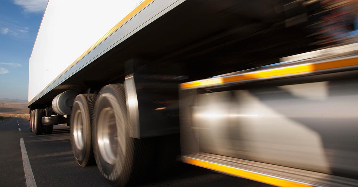 A tractor trailer on the road with a blur in the foreground. 