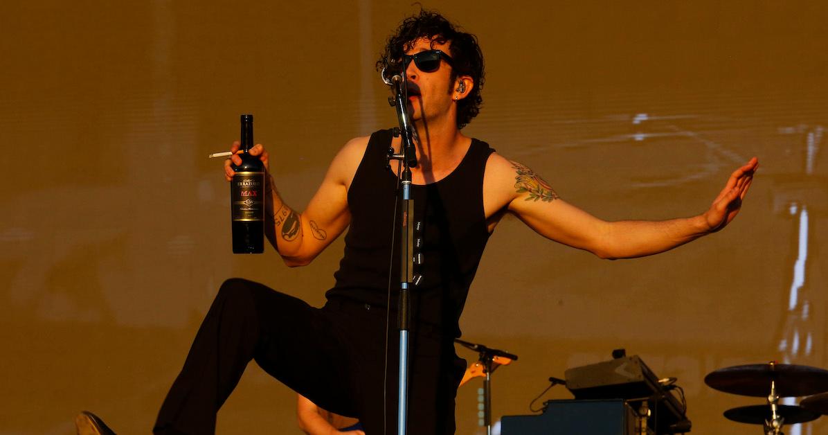 Matty Healy performing onstage while holding a bottle of alcohol