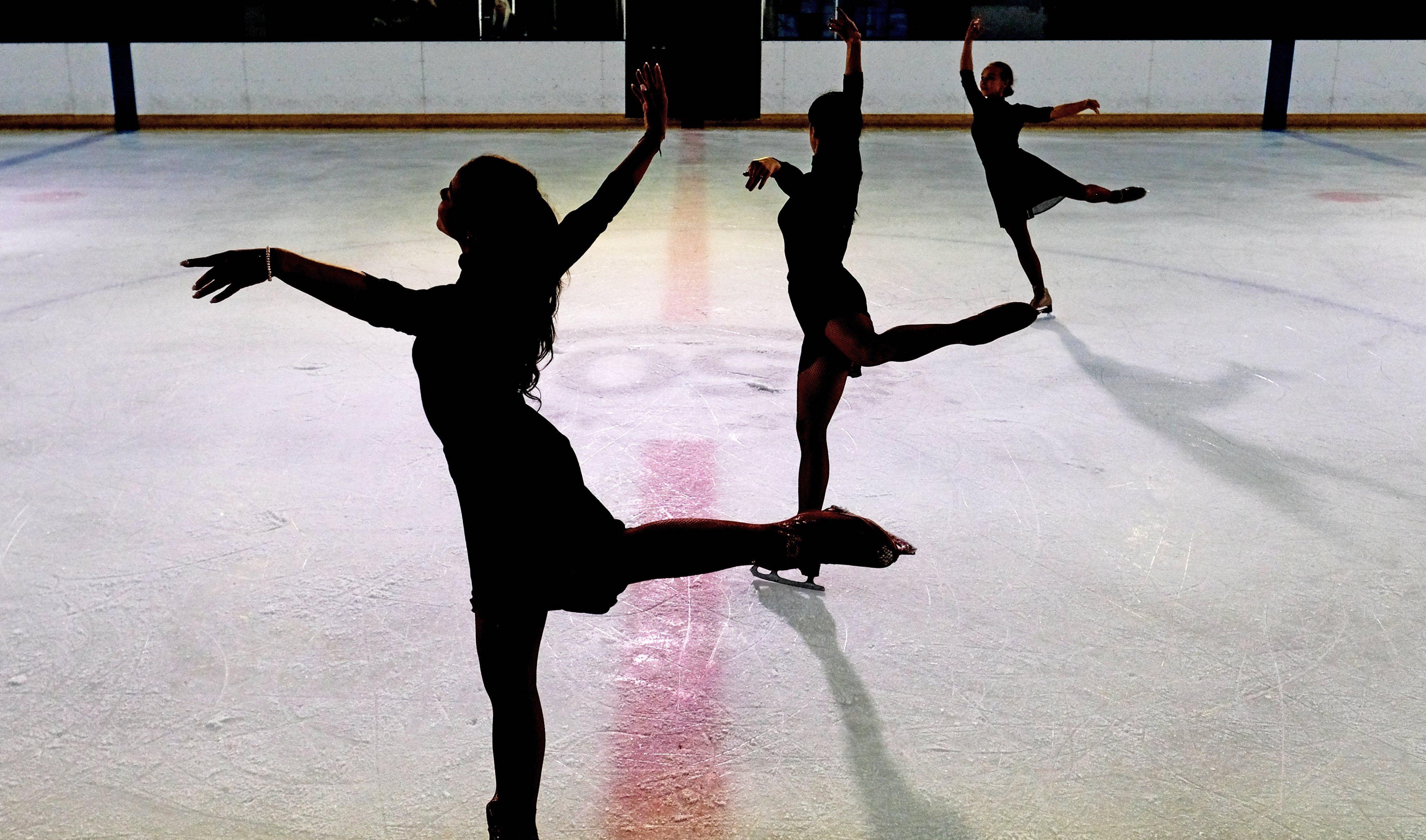 Three figure skaters practice their technique on the ice.