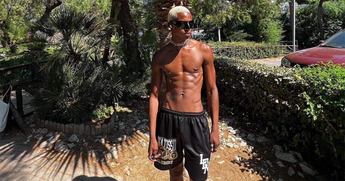 MoDou Adams in sunglasses and black shorts in front of a palm tree. 