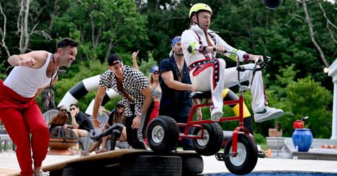 (L-R) Kyle Cooke rides a tricycle into a pool as Carl Radke, Jesse Solomon, and Craig Conover smile and watch in Season 8 of 'Summer House.'