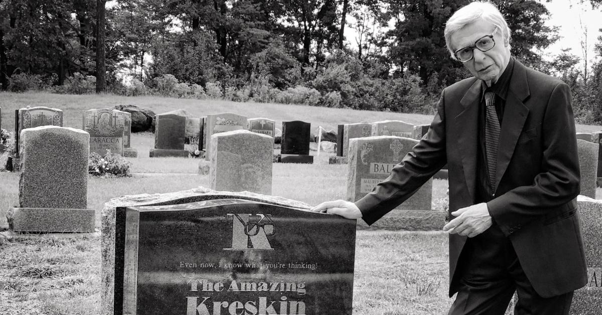 The Amazing Kreskin in a graveyard next to his tombstone.