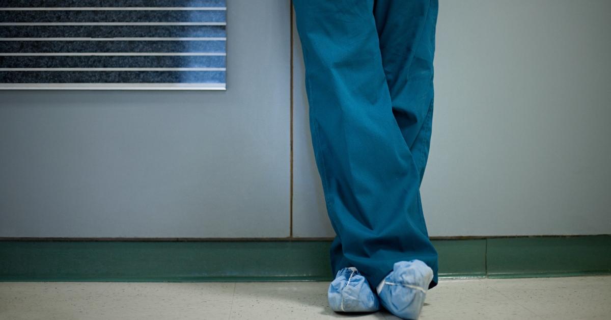 A person in scrubs leaning against the wall.