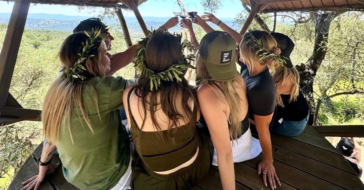 women wear olive leaf crowns and sit in a treehouse toasting