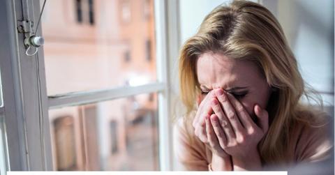 Image of woman crying next to a window.