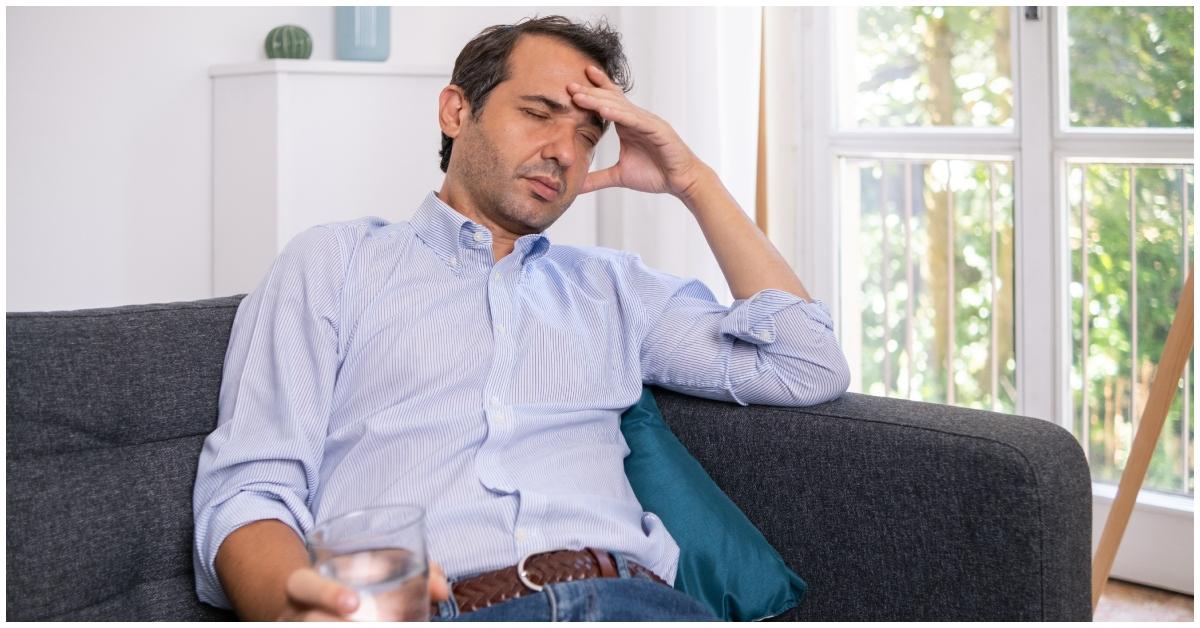 A man holding a glass of water with a headache.