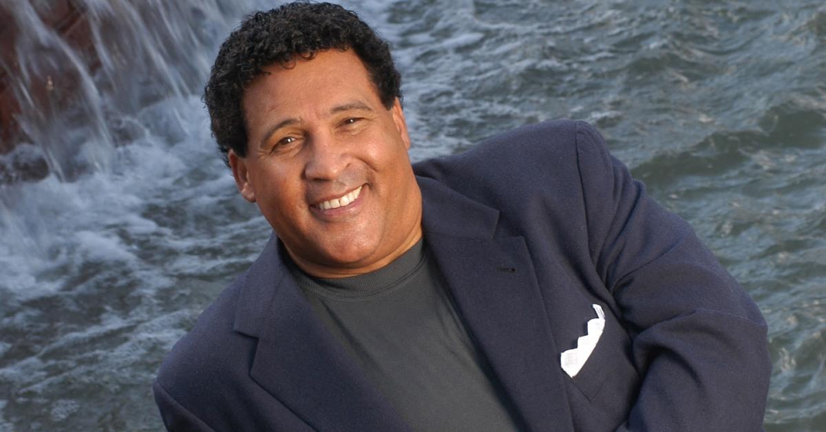 Greg Gumbel posing in front of a waterfall.