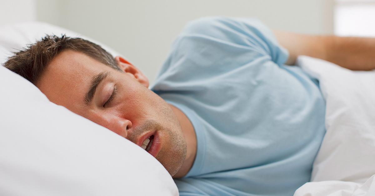 Man sleeping with his mouth open in a bed. 