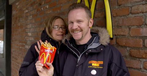 Morgan Spurlock holding McDonald's fries in front of a McDonald's.