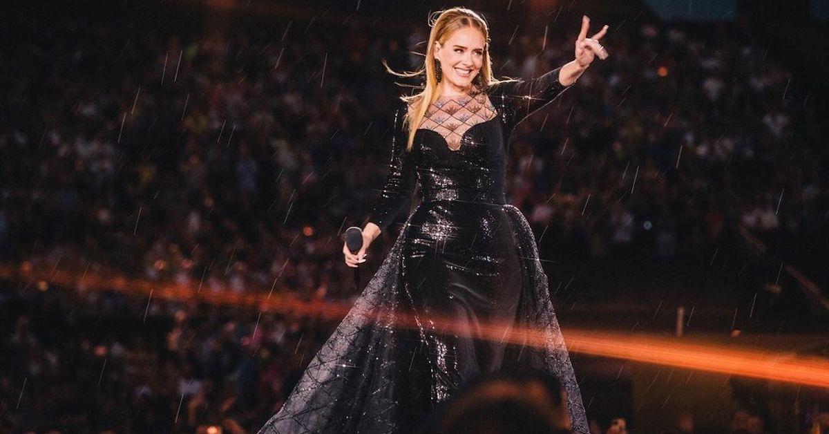 Adele in a black gown on stage, waving at fans