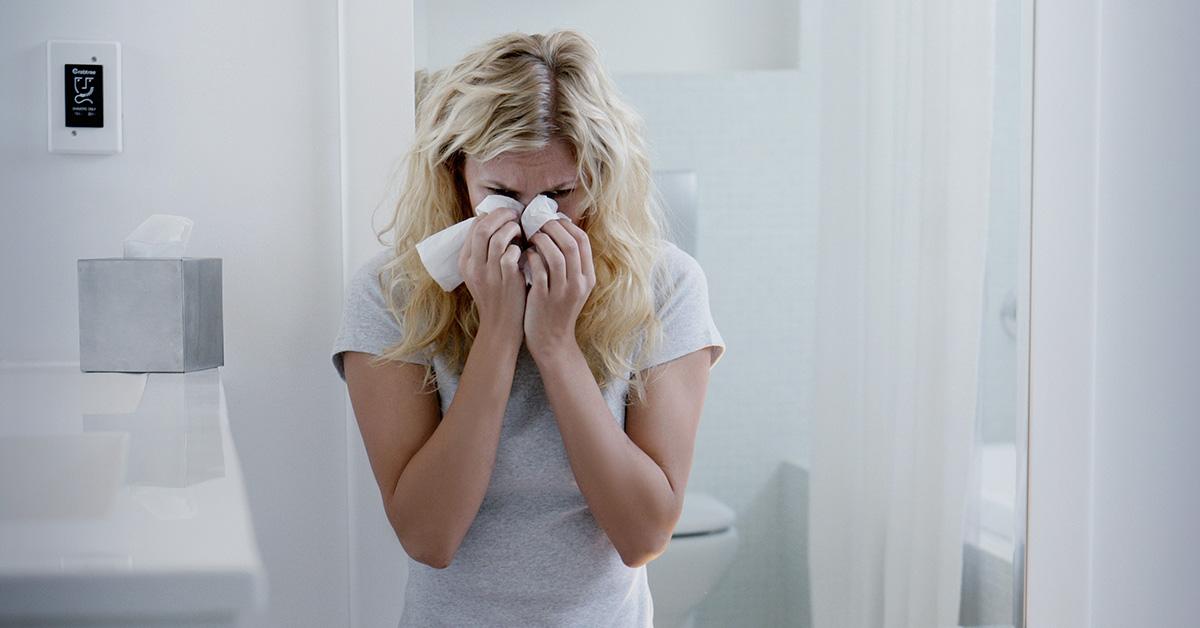 A woman crying into a tissue in a bathroom. 