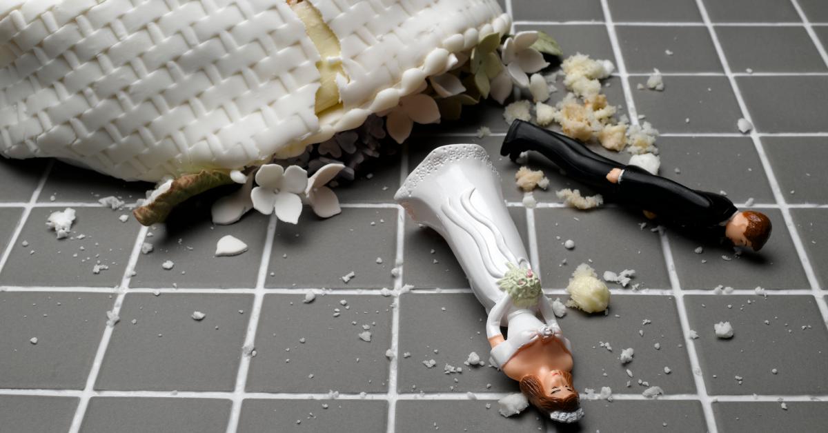 Bride and groom figurines lying near destroyed wedding cake on tiled floor.