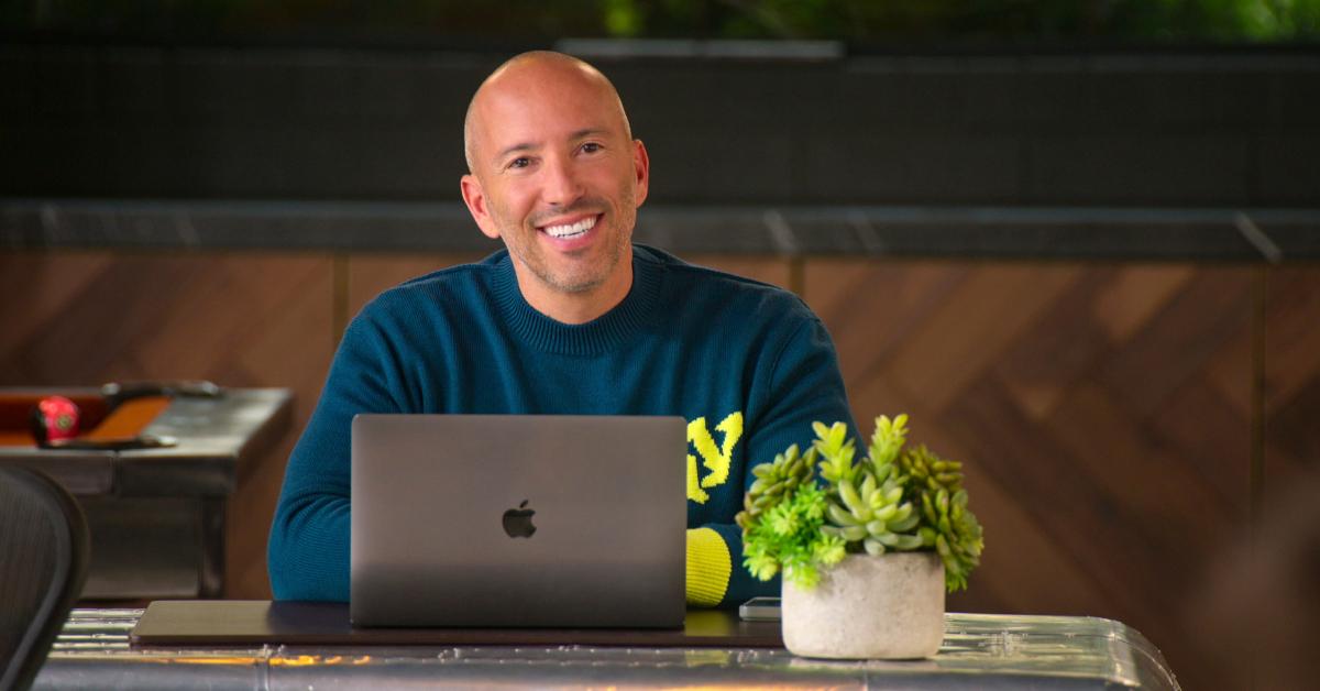 Jason Oppenheim, u plavom džemperu, smiješi se ispred svog laptopa u 'Selling the OC'.