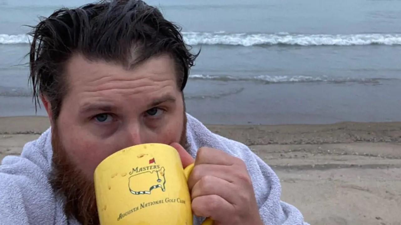 Donovan Eckhardt drinking out of a yellow coffee mug on the beach. 