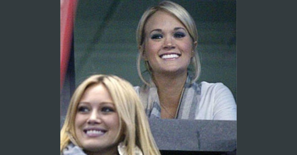 Hilary Duff sitting in front of Carrie Underwood in a hockey arena. 