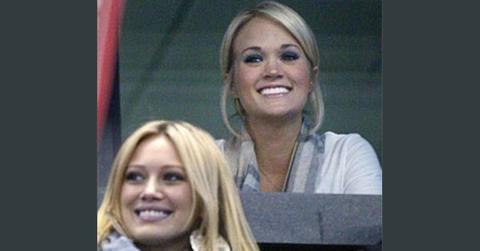 Hilary Duff sitting in front of Carrie Underwood in a hockey arena.