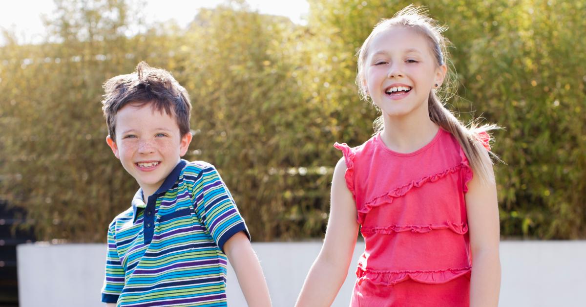 Brother and sister smile while posing for a photo in the backyard.