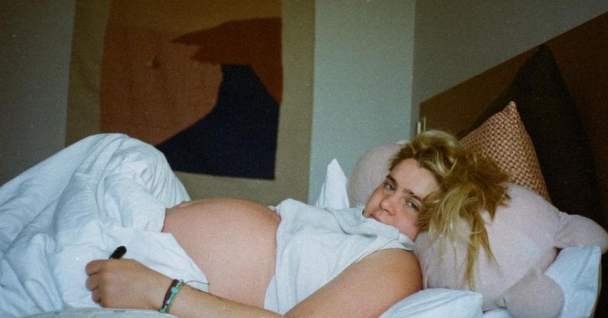 Pregnant Mae Whitman with her baby bump, lying on bed