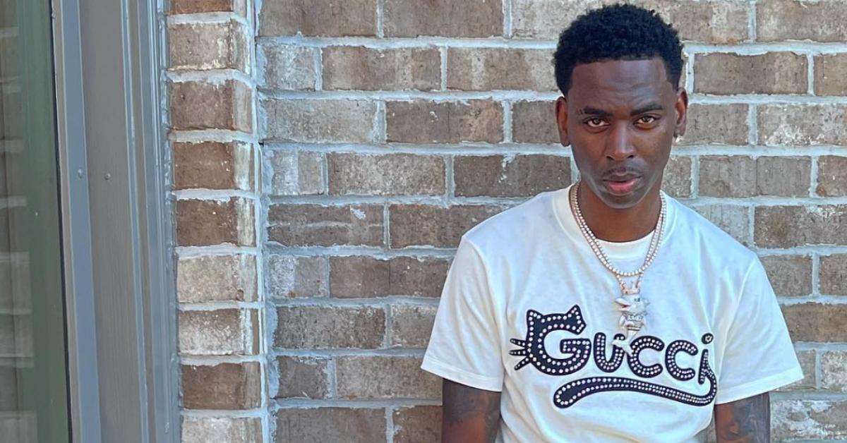 Young Dolph leans against a brick wall