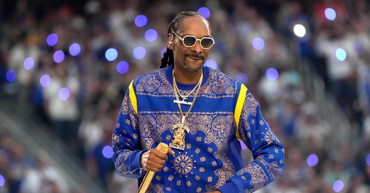 Snoop Dogg wears a blue and yellow sweatshirt with a giant gold Death Row chain. 