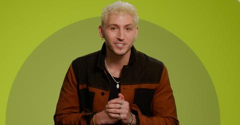 Myles wears a brown and black jacket while posing in front of a green background for 'The Circle' Season 6.