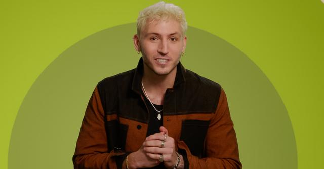 Myles wears a brown and black jacket while posing in front of a green background for 'The Circle' Season 6.