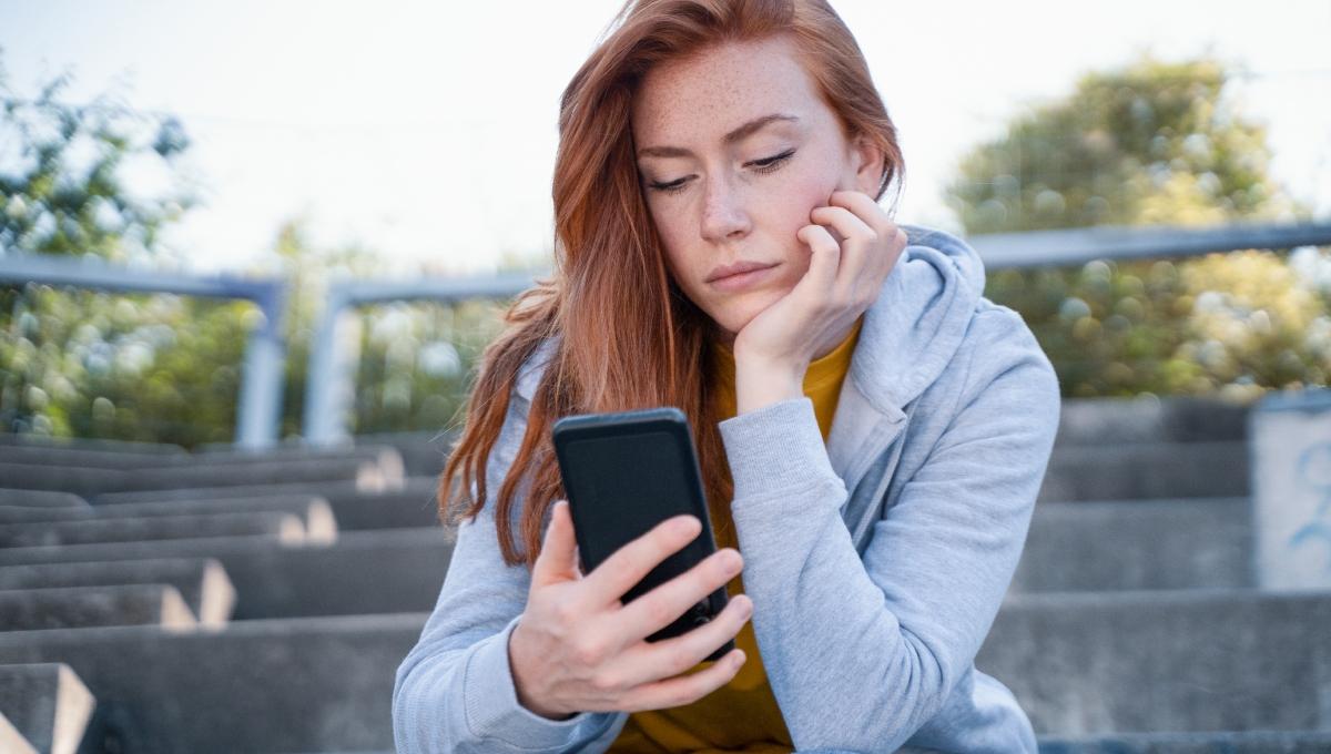 Worried young woman holding mobile phone waiting message