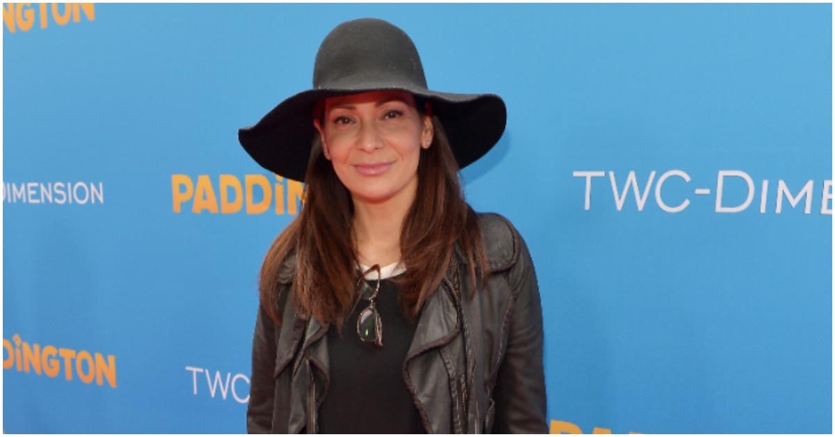 Constance Marie smiling for the camera in a hat and leather jacket.