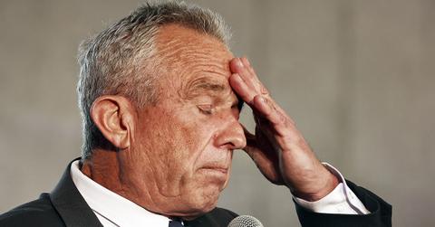 RFK Jr. with his hand on his forehead holding a microphone.