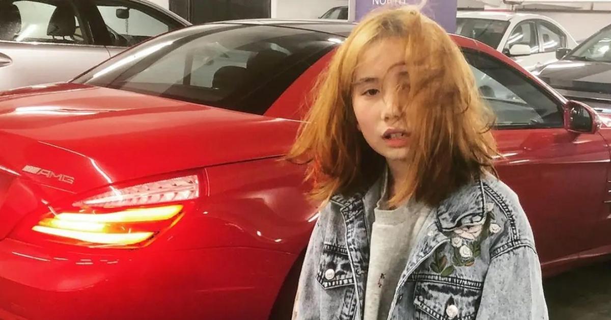 Lil Tay standing next to a red car.