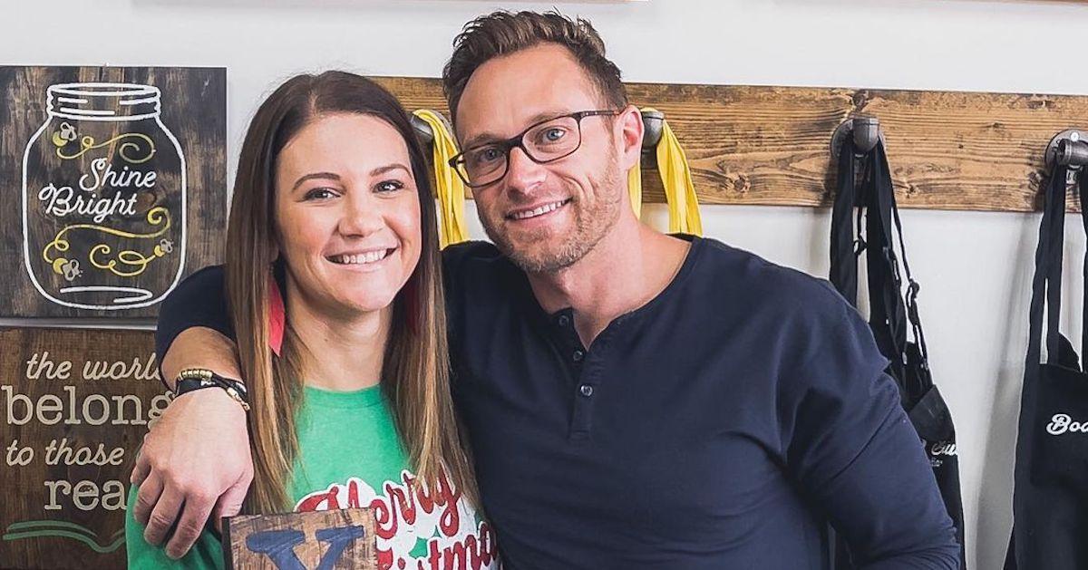 Danielle and Adam Busby stand in front of a wall of aprons