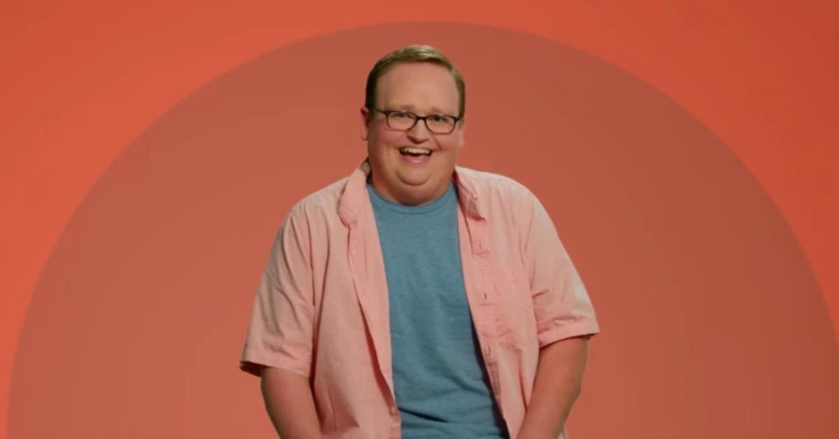Brandon from The Circle smiles in front of an orange background