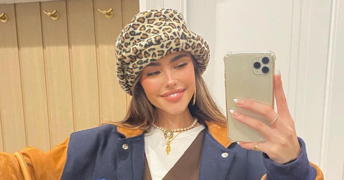 Madison Beer posing for a mirror selfie with a fuzzy cheetah print bucket hat on. 