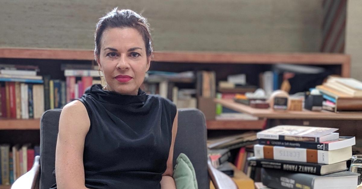 Dr. Orna Guralnik wearing a black dress sitting beside a stack of books. 