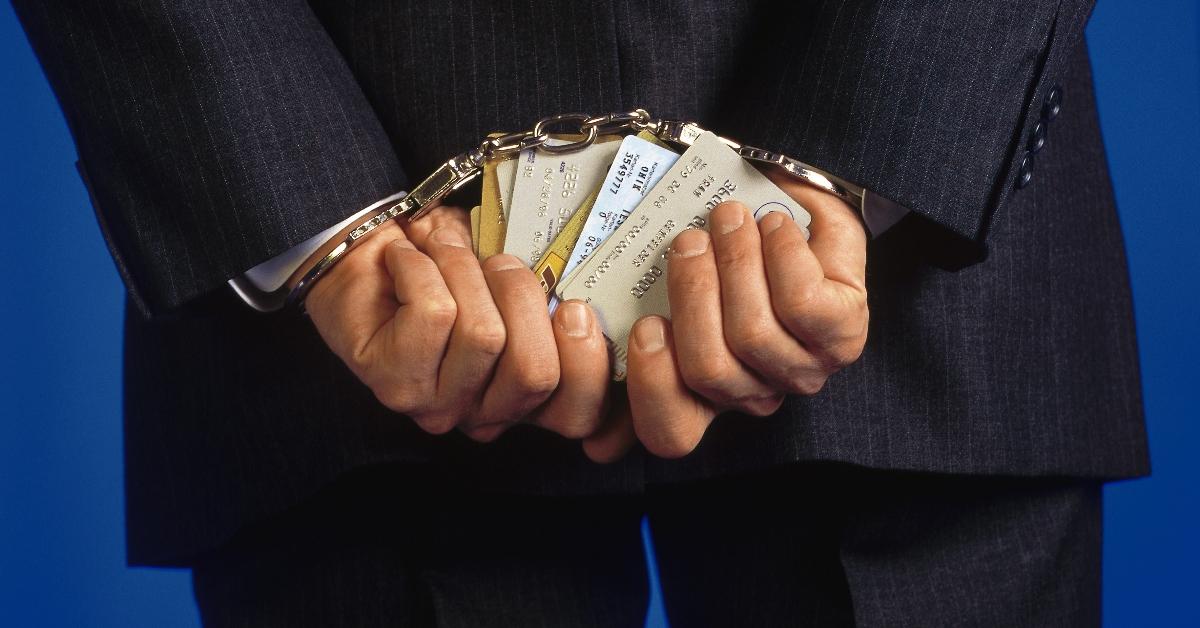 A handcuffed man holds several credit cards