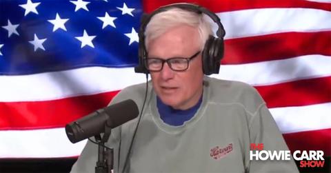 Howie Carr using a mic and headphones with an American flag behind him
