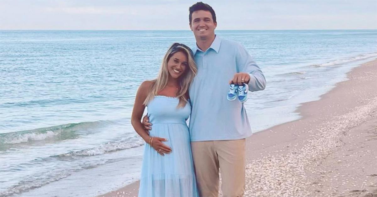 Drew and Natalie Lock on the beach with Drew holding baby shoes. 