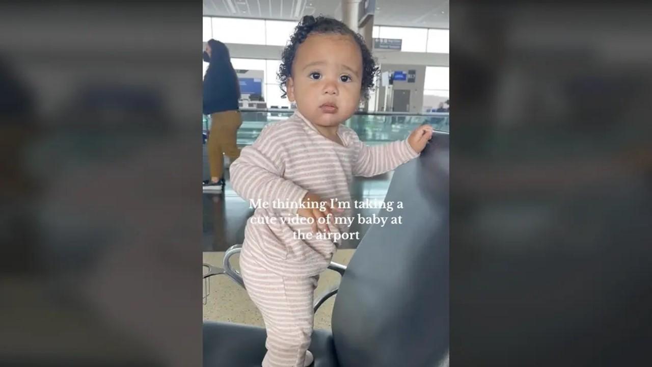 The baby standing on a chair at the airport and looking at her mom