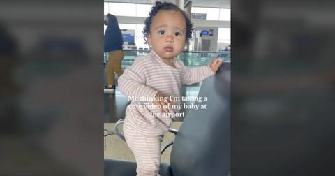 The baby standing on a chair at the airport and looking at her mom