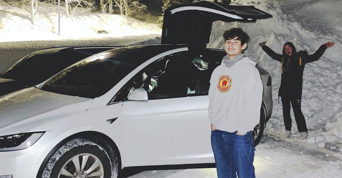 Alek Olsen standing in the snow next to an open Tesla. 