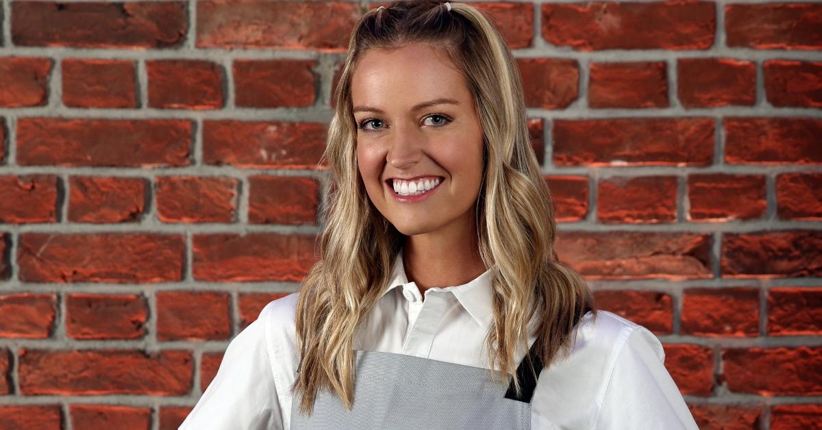 Nicole from Season 3 of 'Next Level Chef' stands in front of a brick wall wearing a gray apron