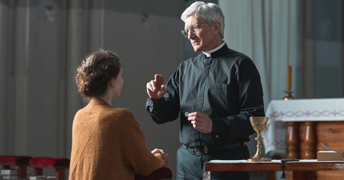 A woman kneels before a priest