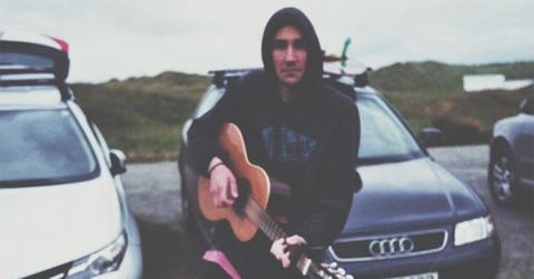 Alek Olsen holding an acoustic guitar with a hood on.