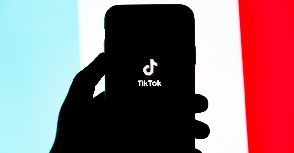 The outline of a hand holding a phone with TikTok on the screen