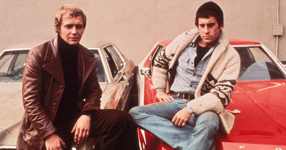 David Soul and Paul Michael Glaser sitting on the hoods of their cars, from the television series, 'Starsky and Hutch,' circa 1977