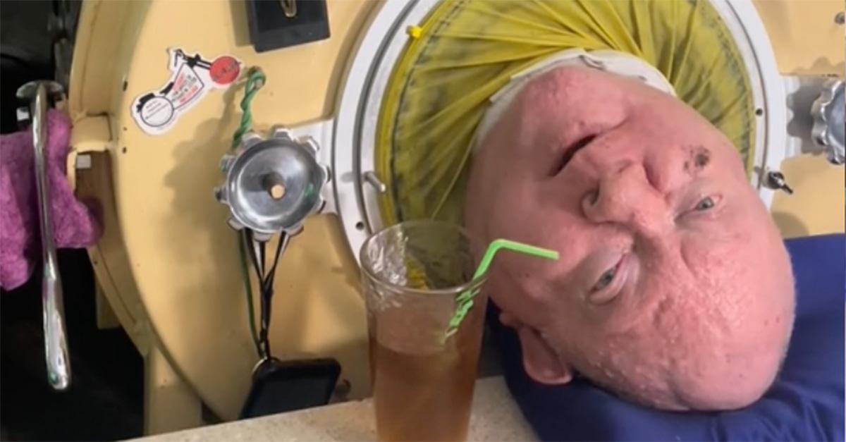 Paul Alexander with a drink near his lips in his iron lung. 