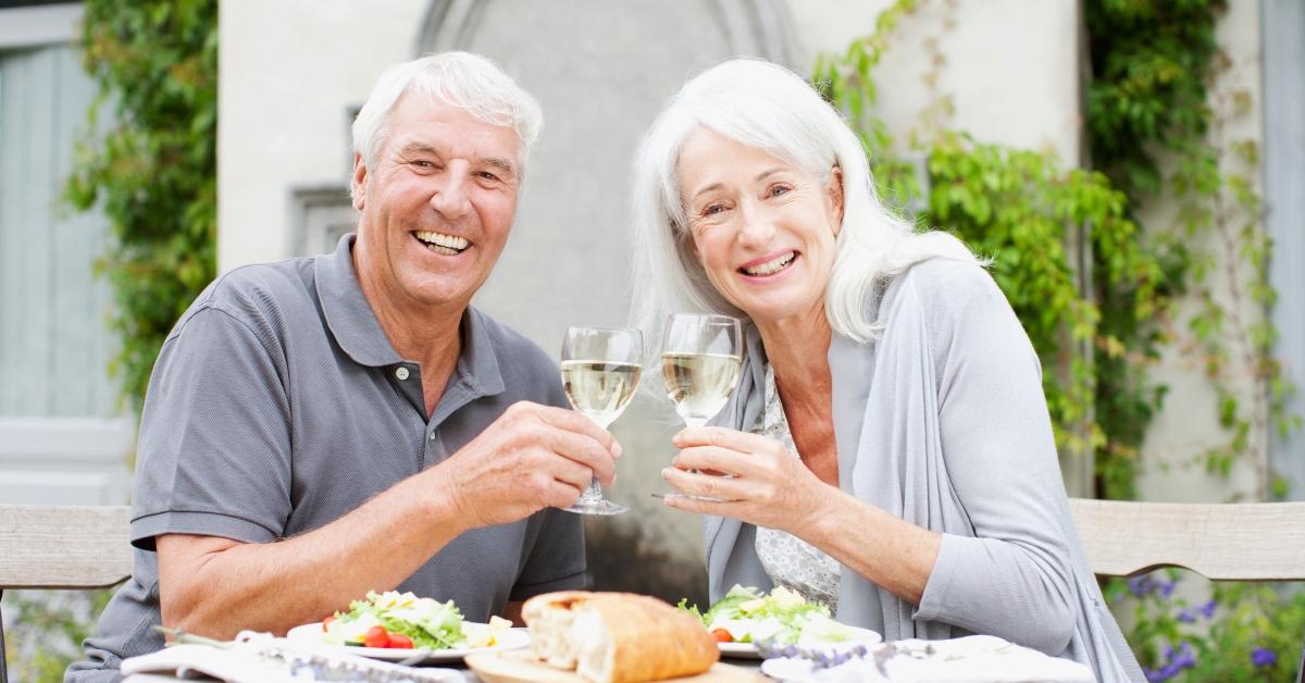 Elderly couple toast wine glasses and smile at lunch.