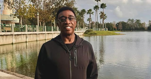 Wayne Dawson wearing a hoodie and standing next to a body of water.